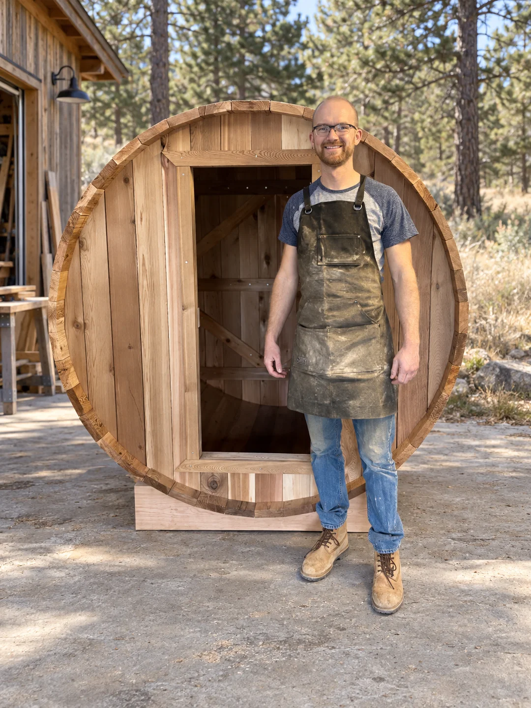Michael, the person behind Saunart, in a work apron beside a barrel sauna he is building